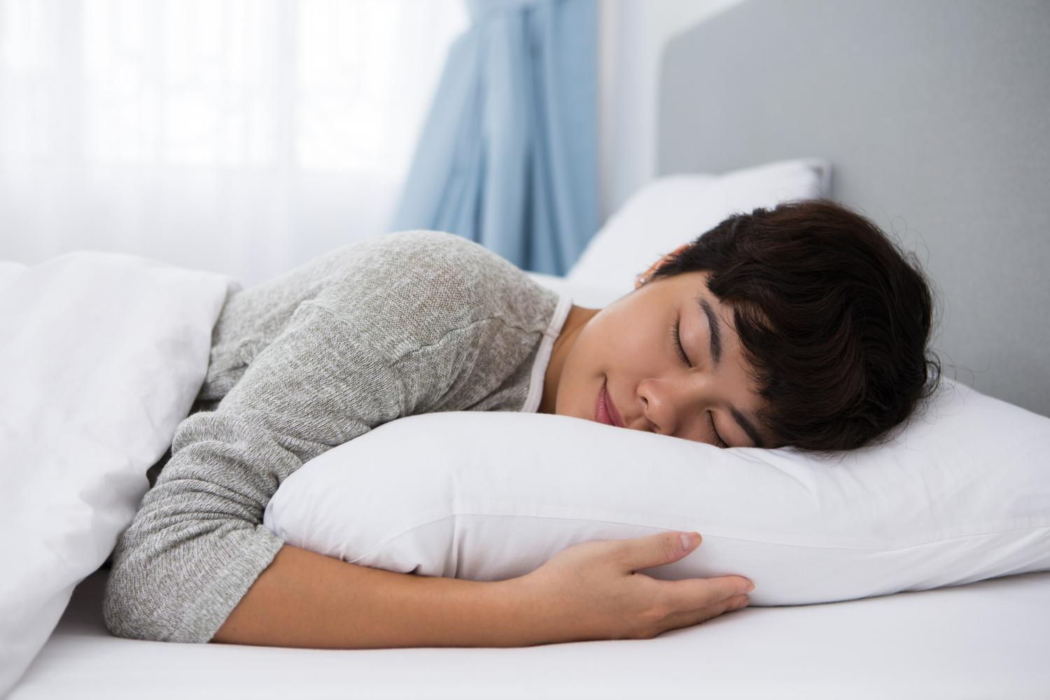 Does Sleeping Burn Calories? Understanding How Sleep Affects Your Metabolism 4 A woman sleeping on her side, resting her head and arm on a white pillow in a bright bedroom.