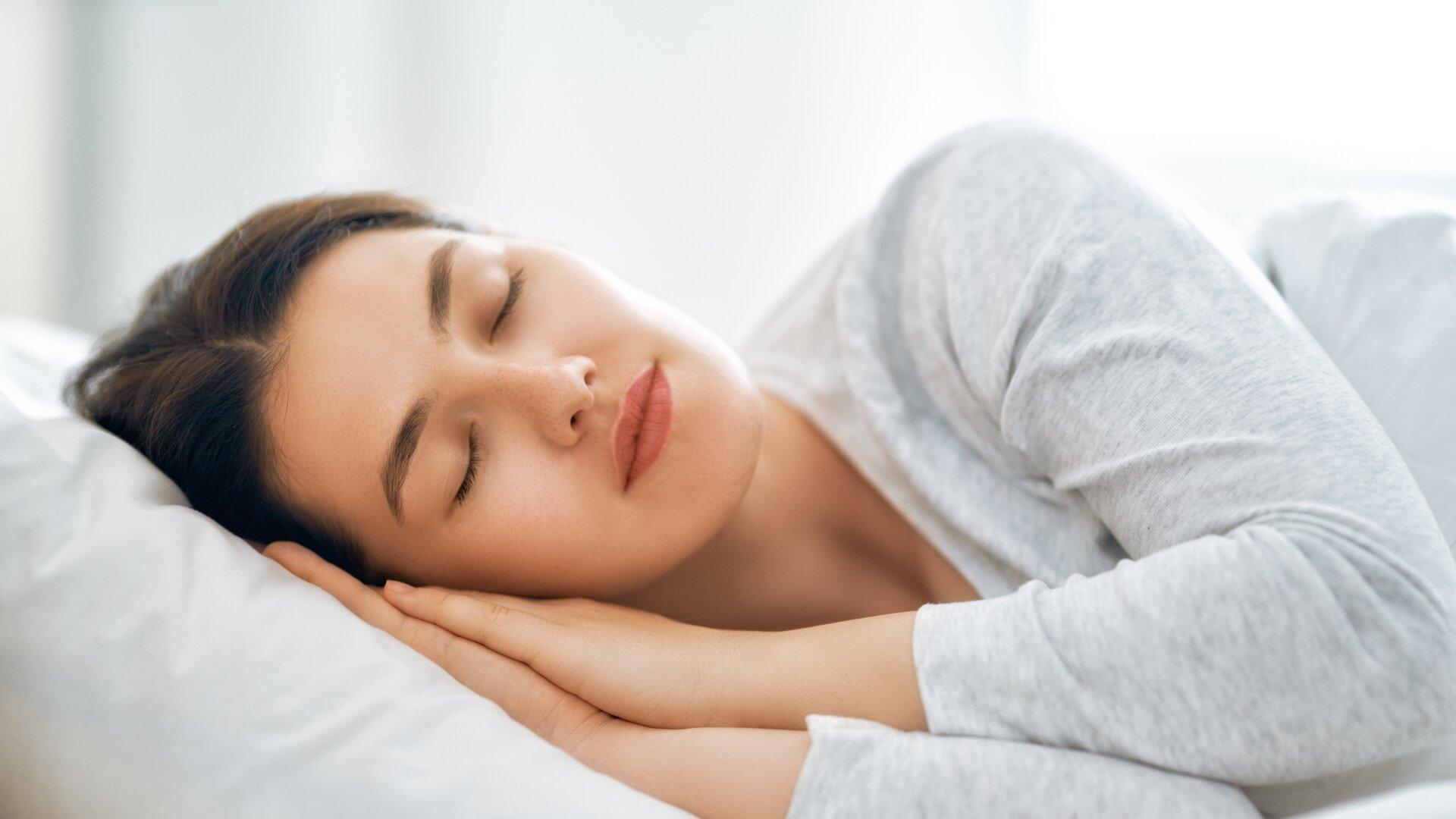 Woman side sleeping peacefully on a white pillow in a bright bedroom.