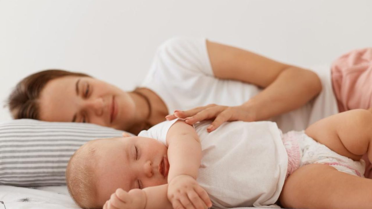 indoor-shot-sleeping-woman-her-charming-small-daughter-lying-bed-with-closed-eyes-resting-afternoon-mommy-looking-baby-with-great-love-hugging-her